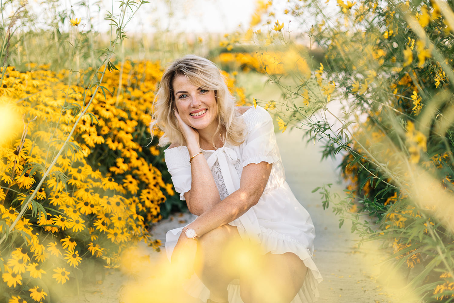 Lifestyle portret van vrouw in witte jurk in tussen gele bloemen voor personal branding