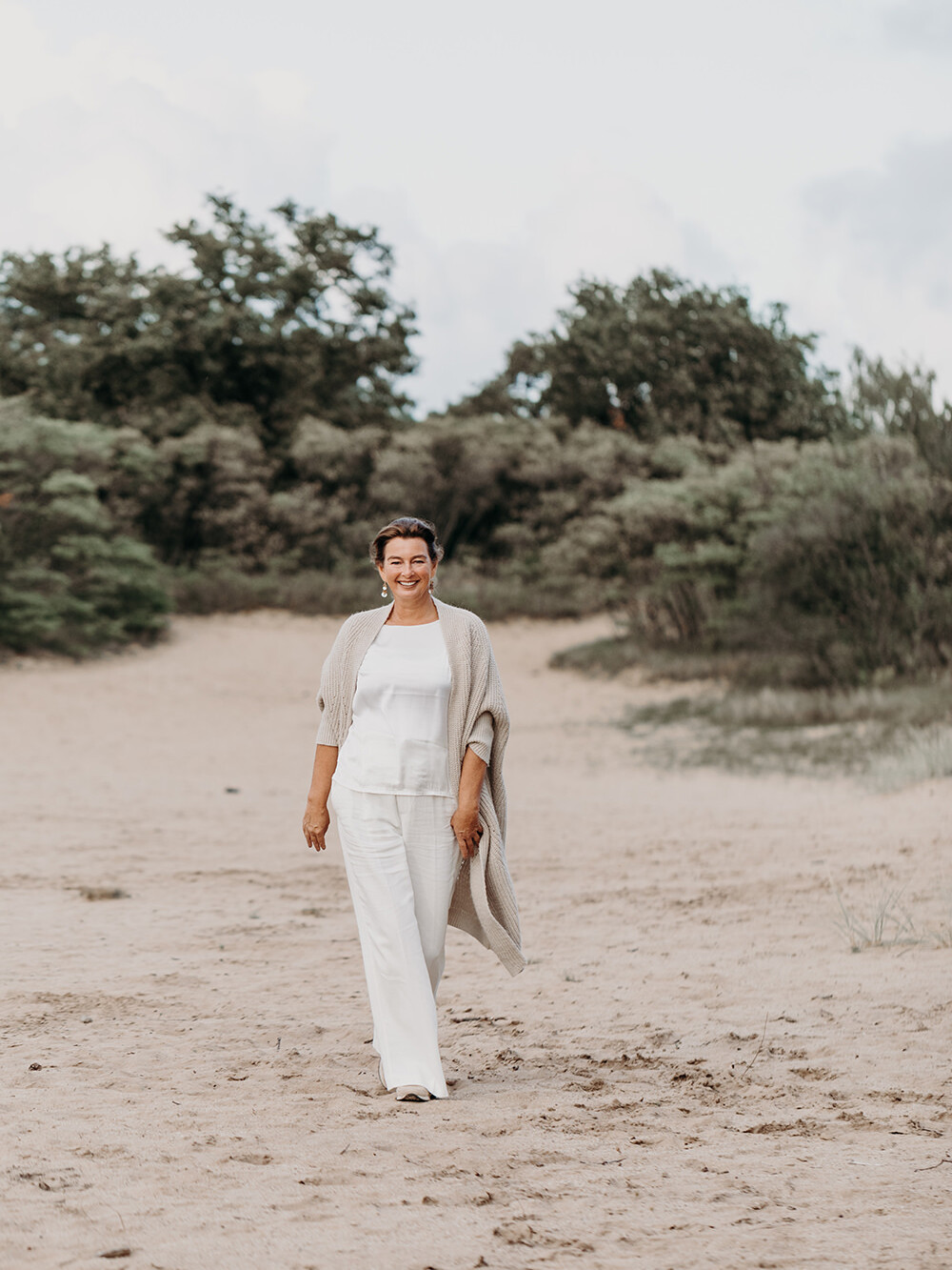 Lifestyle portret van lopend vrouw in witte kleren en vest in de duinen voor personal branding