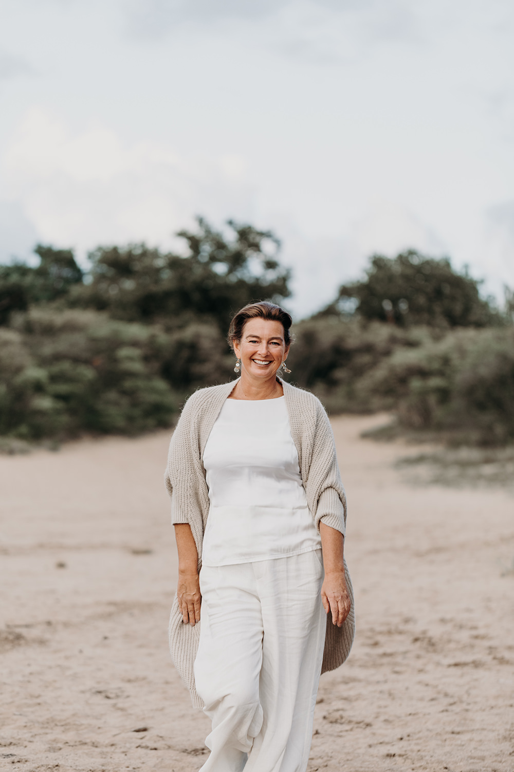 Lifestyle portret van lopend vrouw in witte kleren en vest in de duinen voor personal branding