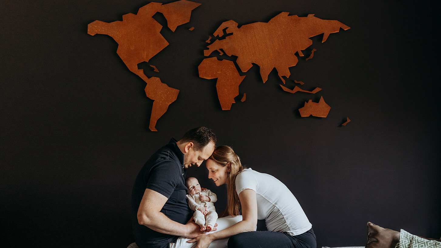 foto van een gezin met een baby en de wereldmap op de muur tijdens een gezinsfotoshoot aan huis