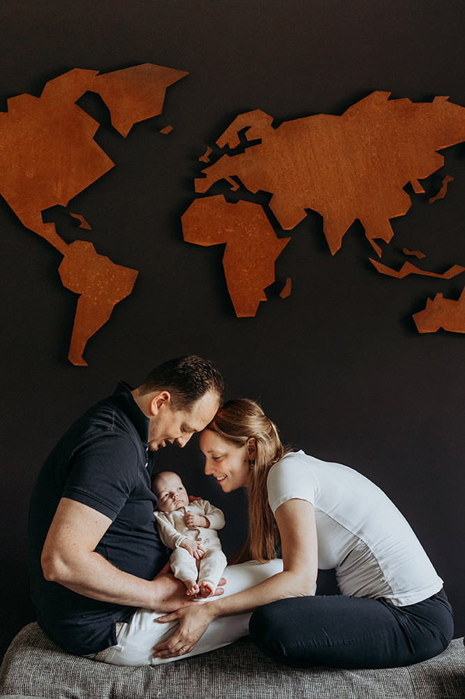 foto van een gezin met een baby en de wereldmap op de muur tijdens een gezinsfotoshoot aan huis