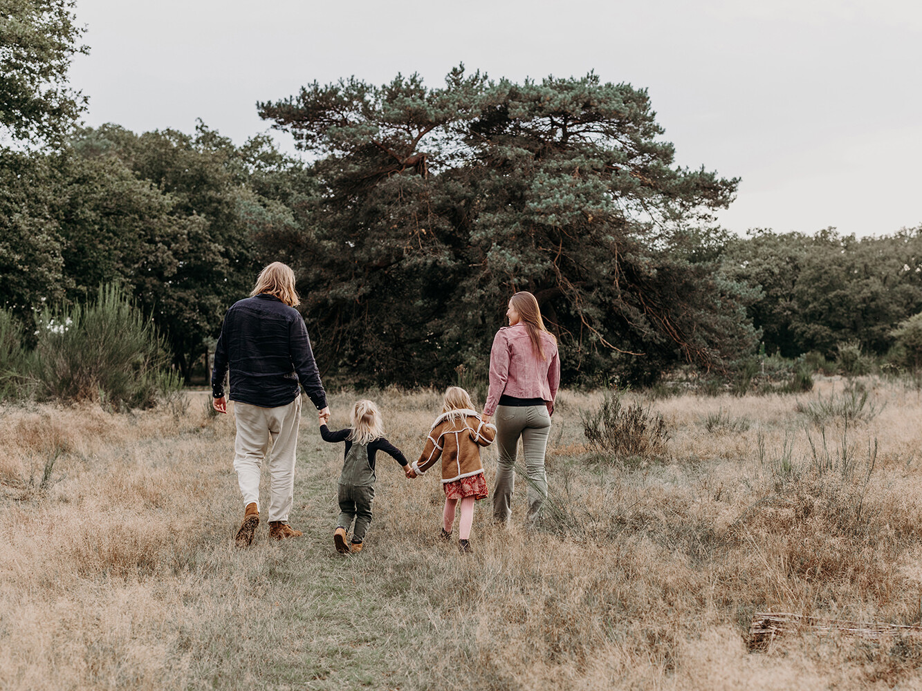 Foto van een hand-in-hand lopend gezin van 4 van achteren tijdens een gezinsfotoshoot buiten