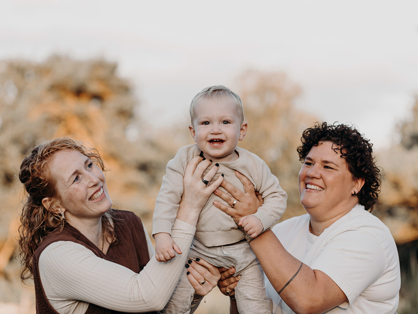 lachende baby in de lucht met zijn moeders tijdens een gezinsfotoshoot buiten