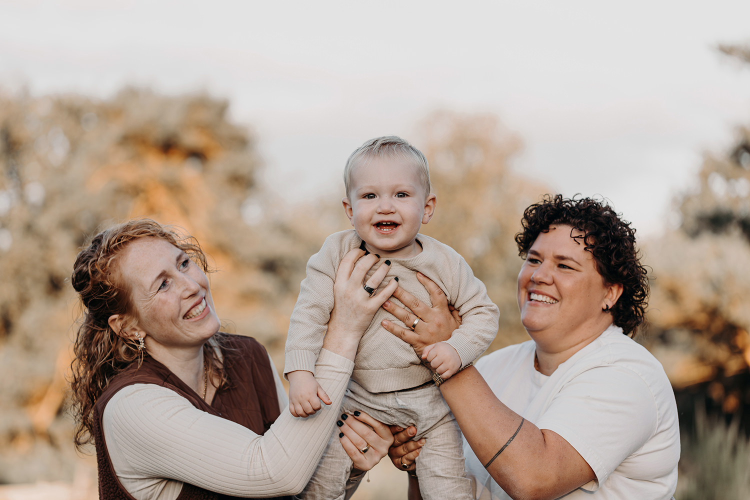 lachende baby in de lucht met zijn moeders tijdens een gezinsfotoshoot buiten