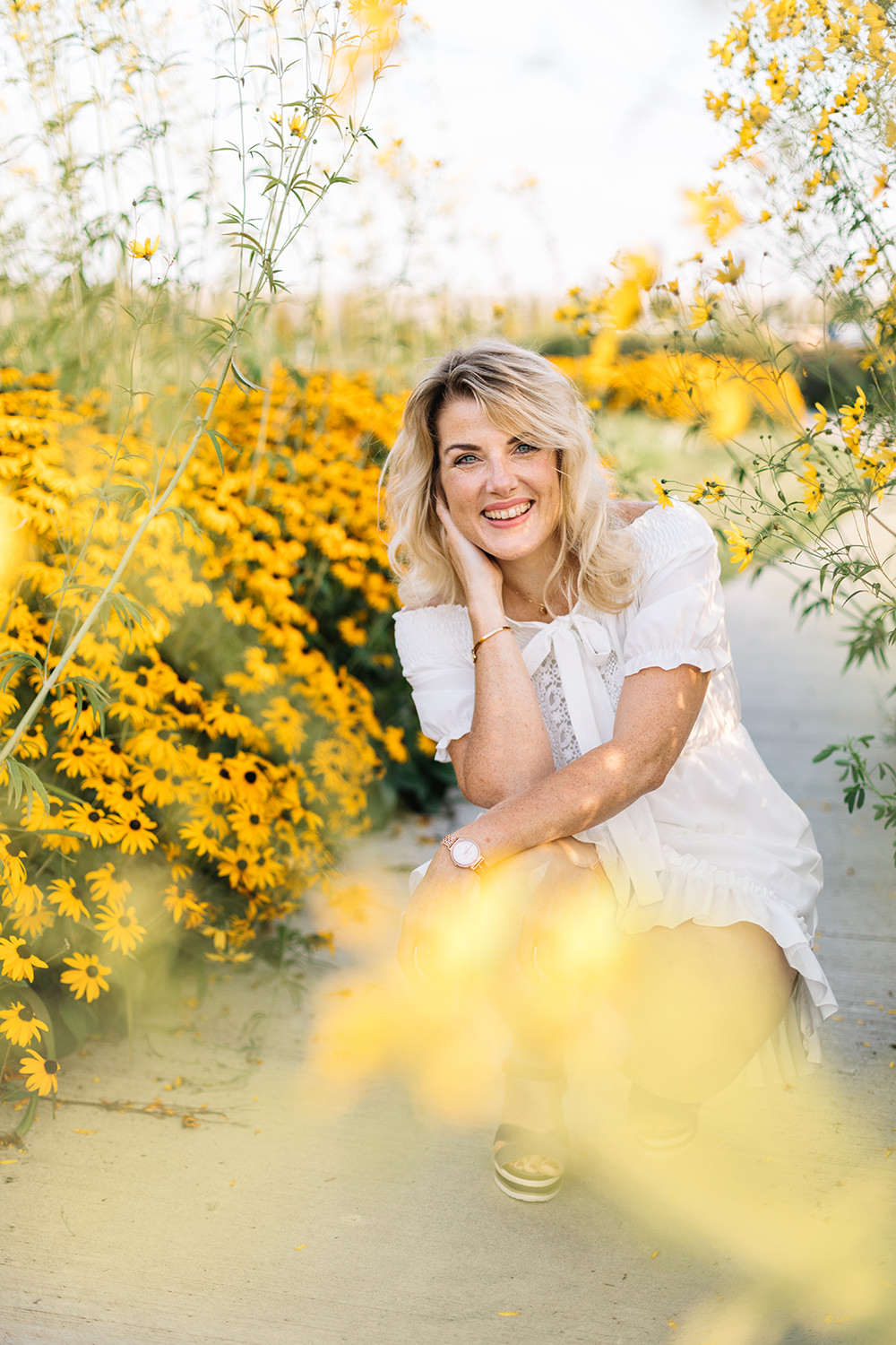 Lifestyle portret van vrouw in witte jurk in tussen gele bloemen voor personal branding