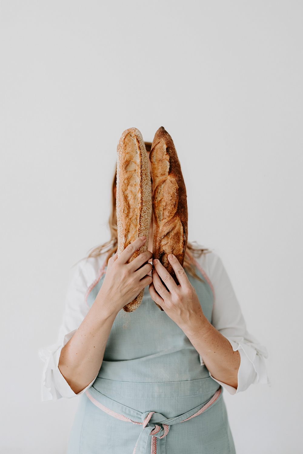 Lifestyle foto van een vrouw die twee baguettes voor haar gezicht houdt voor een personal branding fotoshoot