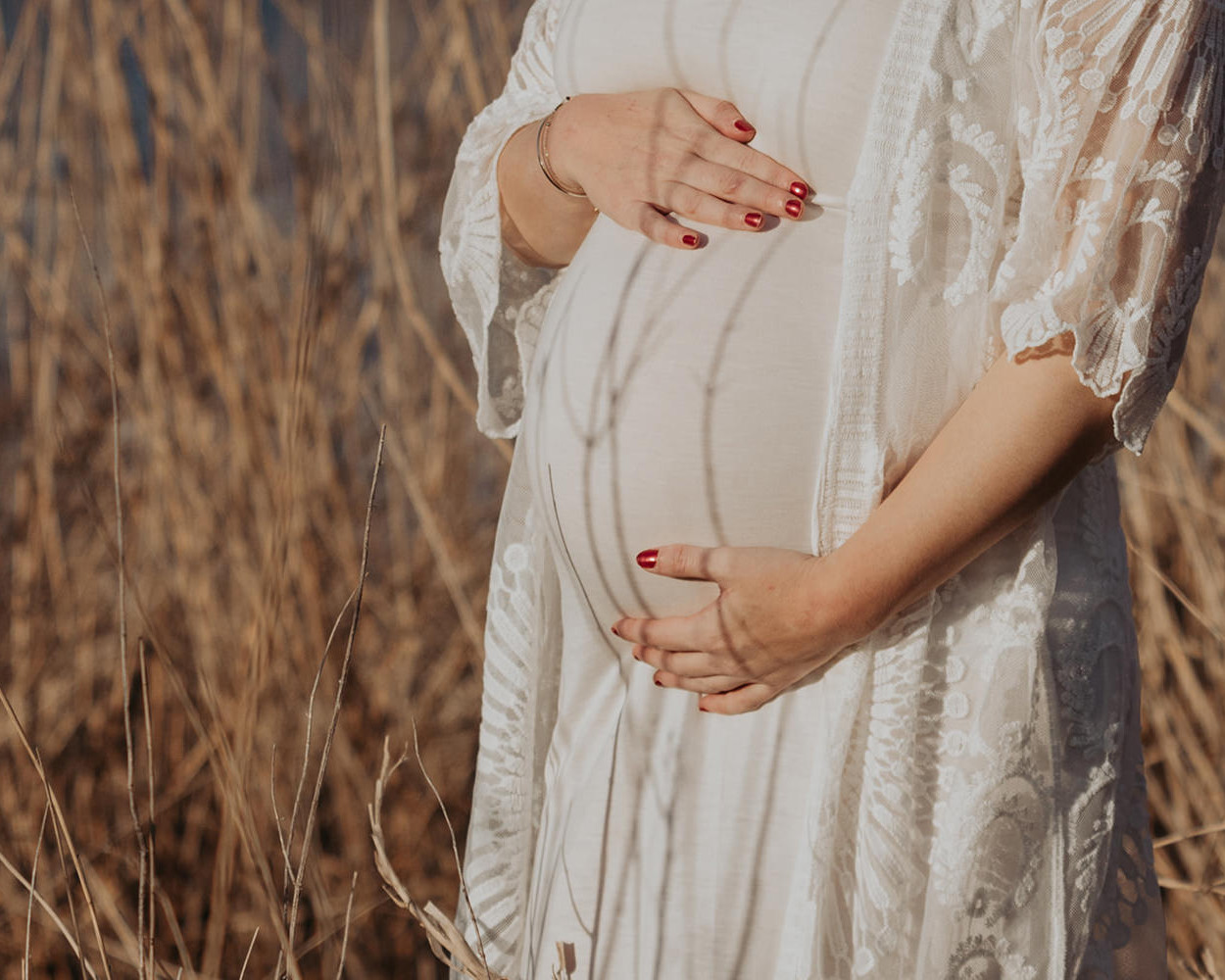 Kleurenfoto van een zwangere buik, vrouw in een witte jurk tijdens een zwangerschapsfotoshoot