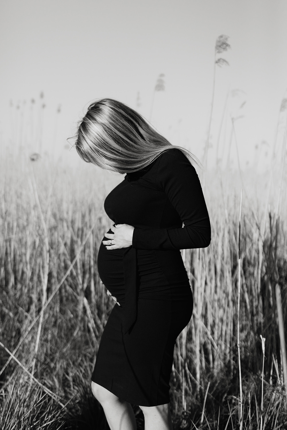 zwart-wit foto van een jonge zwangere vrouw met lang blond haar tijdens een zwangerschapsshoot buiten op locatie