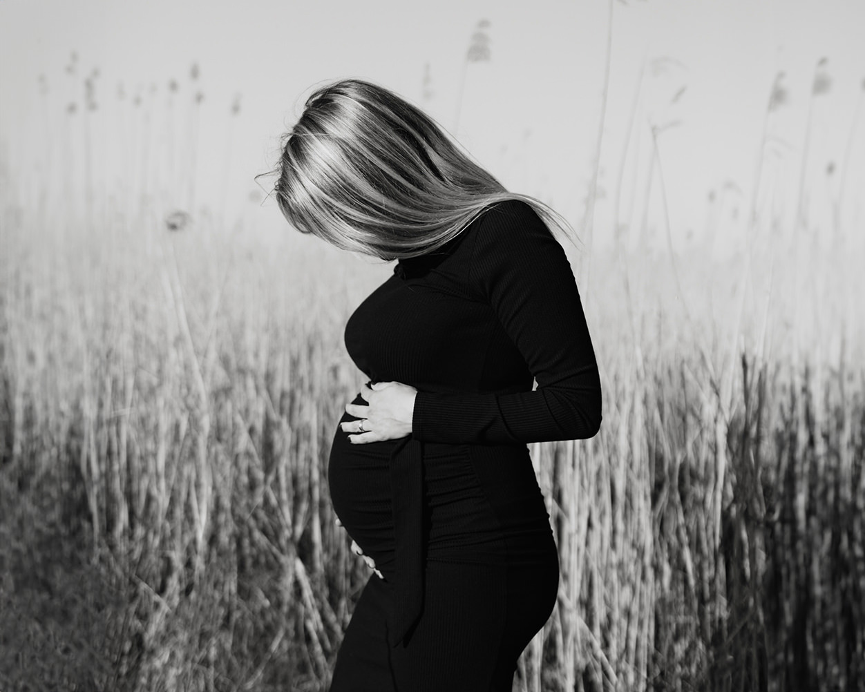 zwart-wit foto van een jonge zwangere vrouw met lang blond haar tijdens een zwangerschapsshoot buiten op locatie